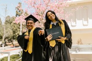 Joyful male and female graduates celebrate their graduation outdoors with diplomas.