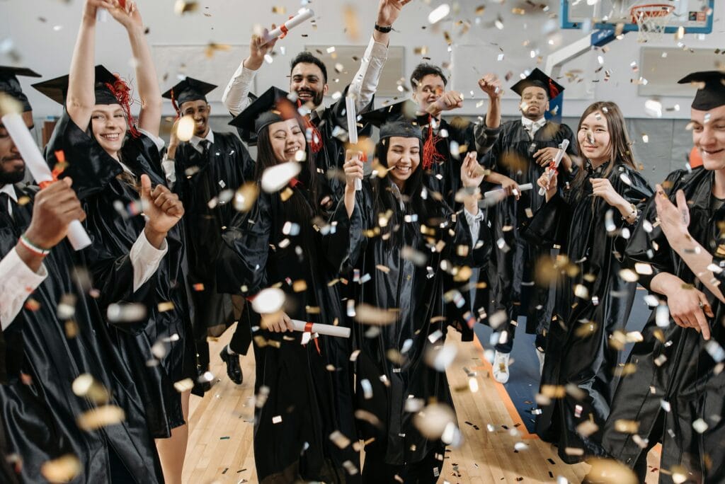 A diverse group of graduates celebrating with confetti indoors, capturing achievement and joy.